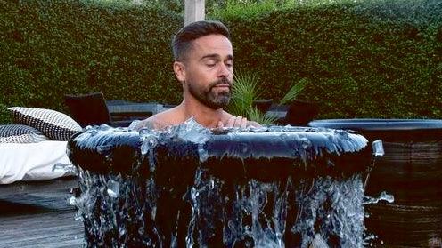 Homem relaxando em banheira de imersão fria para recuperação pós-treino com água escorrendo