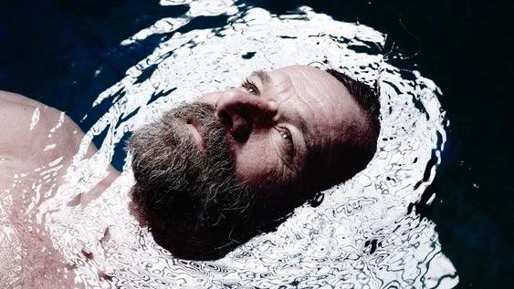Homem com barba flutuando na água, recuperação pós-treino com imersão fria